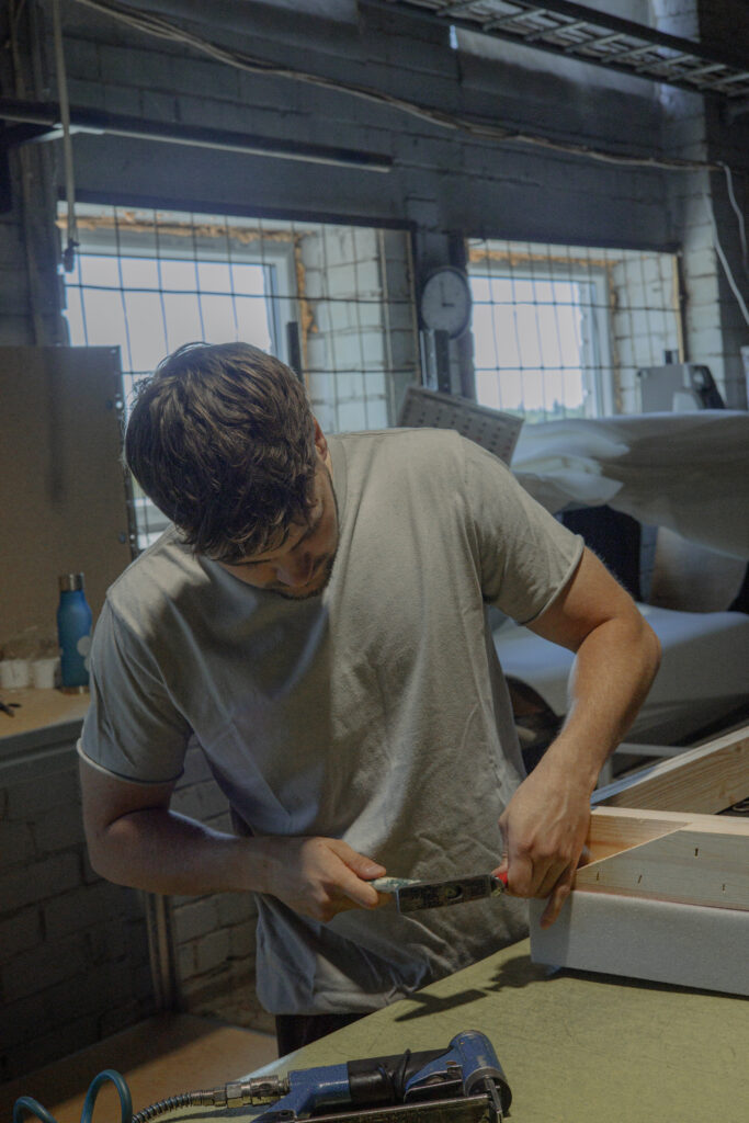 A production worker tightens a wooden structural part during furniture assembly.
